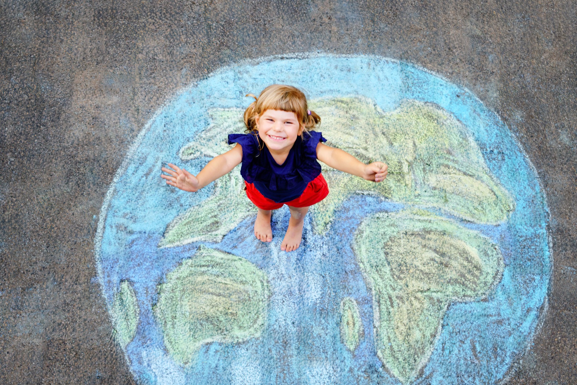 Little preschool girl with earth globe painting with colorful chalks on ground. Positive toddler child. Happy earth day concept. Creation of children for saving world, environment and ecology.